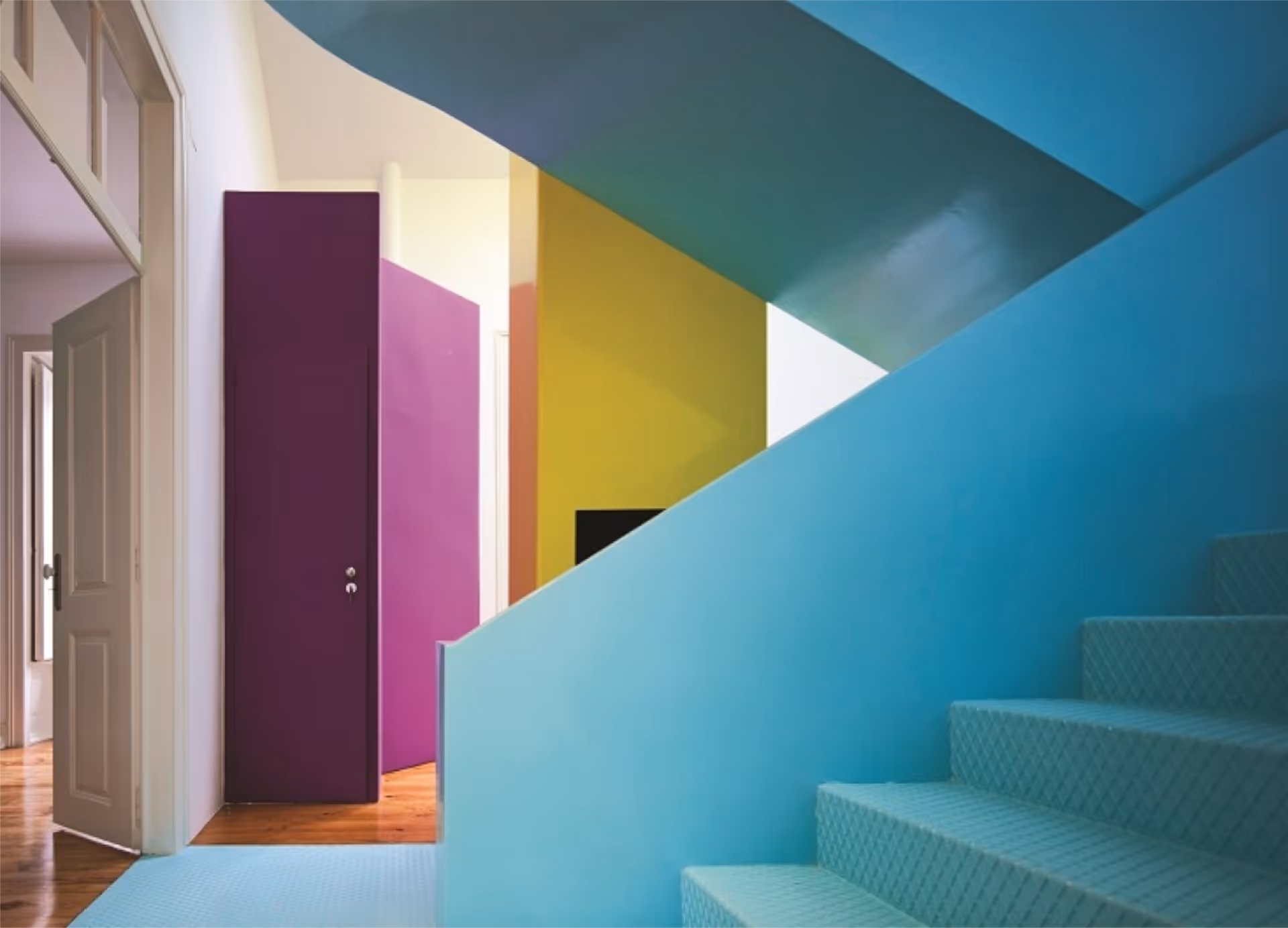A hall and stairway with bright colour blocking on the walls in colours of turquoise, pink and lime green.