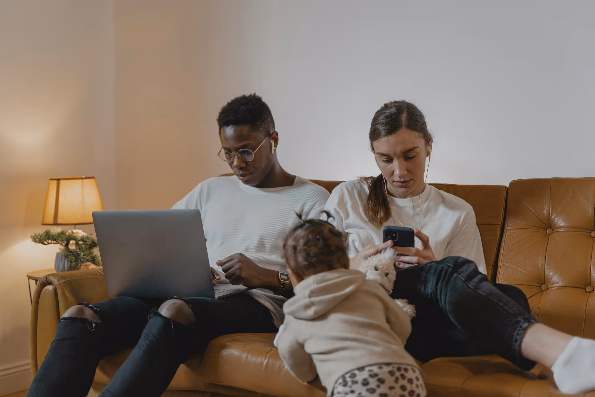 Parents sitting on a sofa, busy on their electronic devices whilst their child would like some attention.