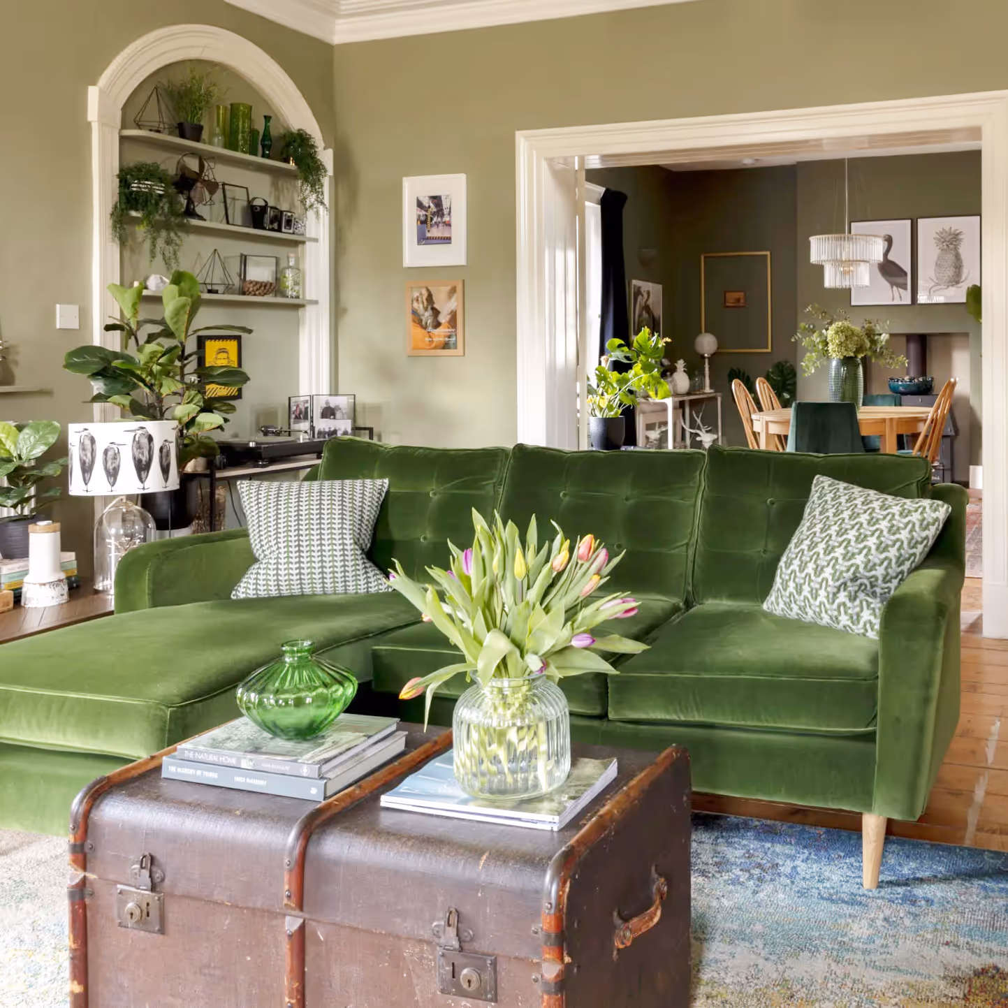 A biophilic designed interior for a living room with green walls, a green velvet sofa and lots of plants.