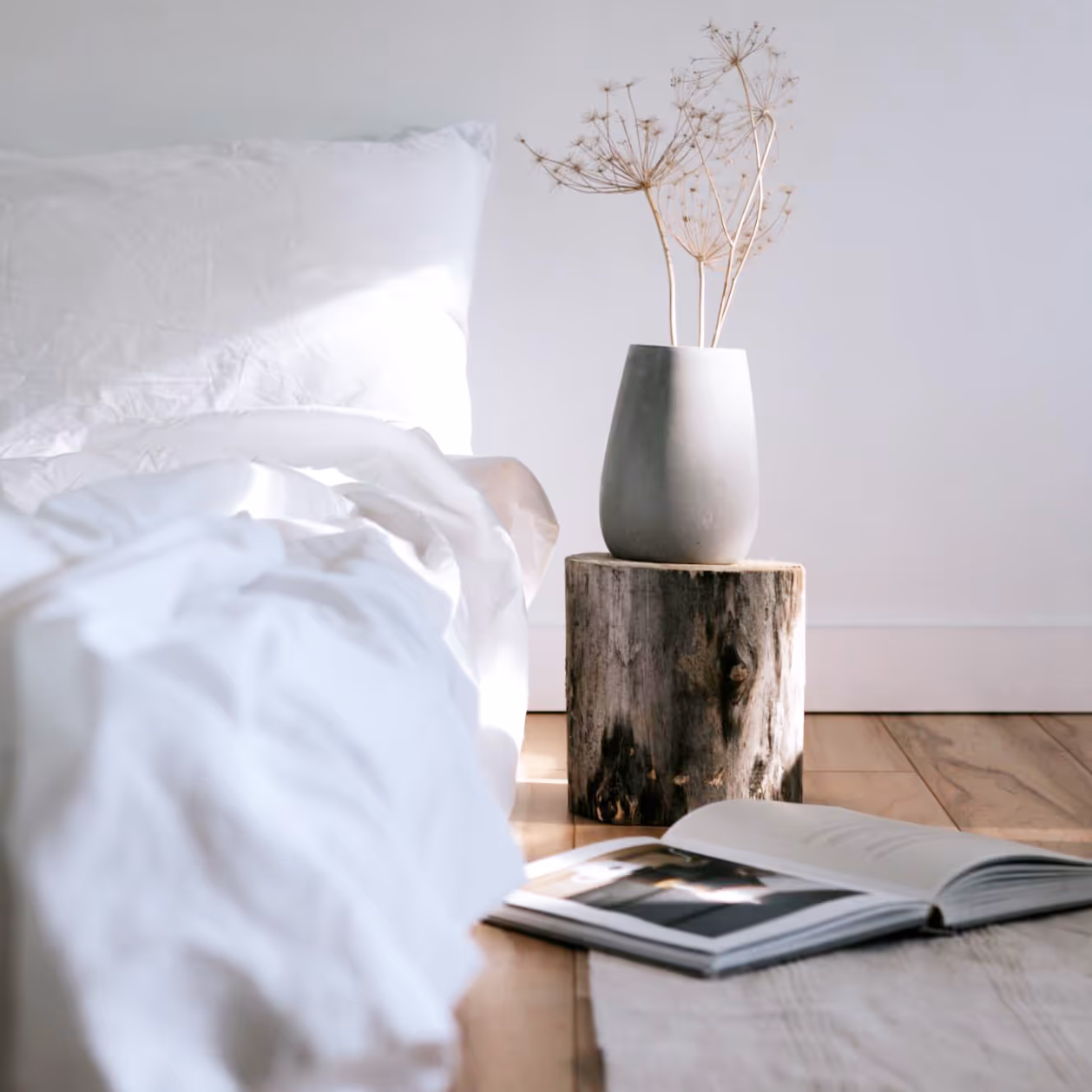 A simple white bedroom with a wooden floor and a simple upturned log as a bedside table.