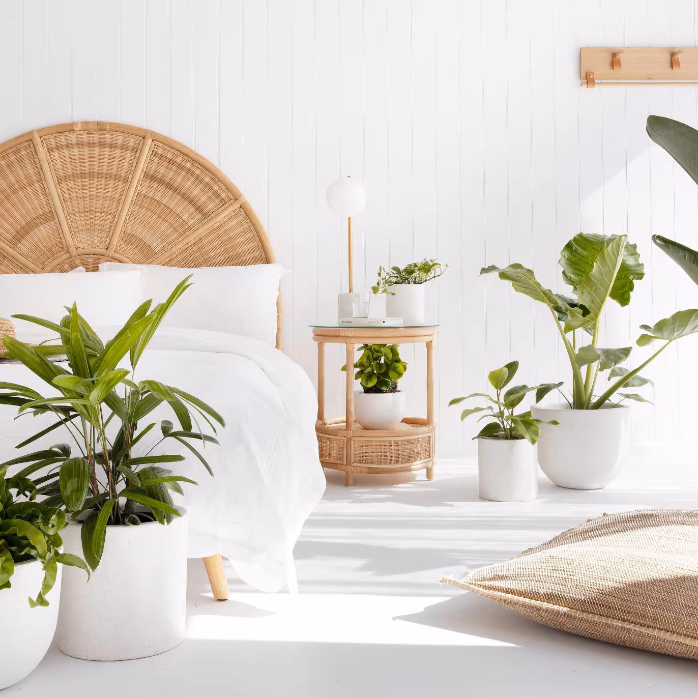 A white bedroom with rattan furniture and houseplants.