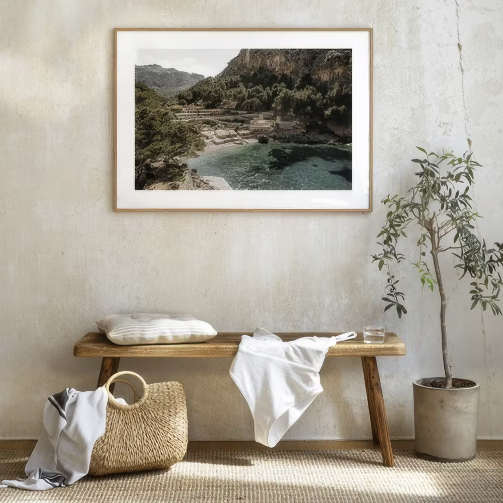 A wooden bench and basketware against a rough plastered wall with a framed photo of a rocky cove.