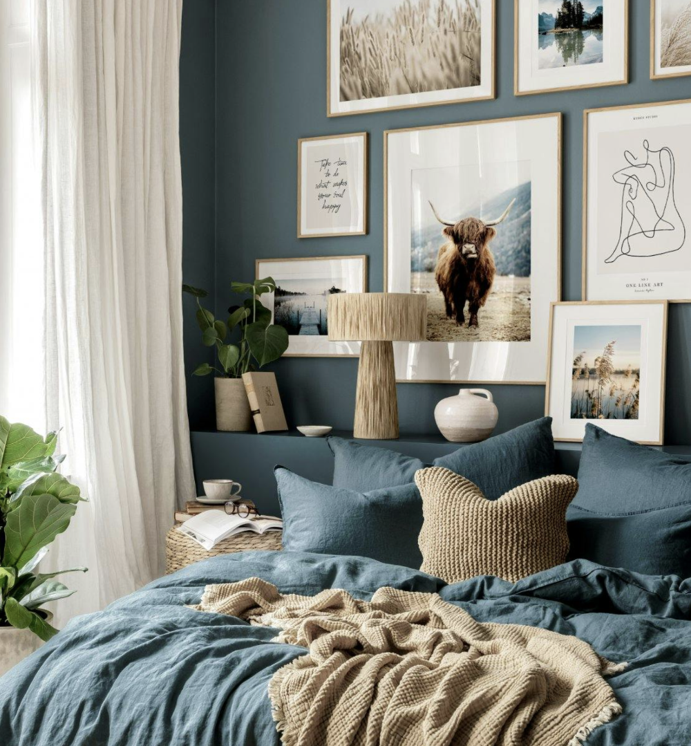 A blue bedroom with lightweight sheer curtains and a wall of assorted framed pictures depicting nature.