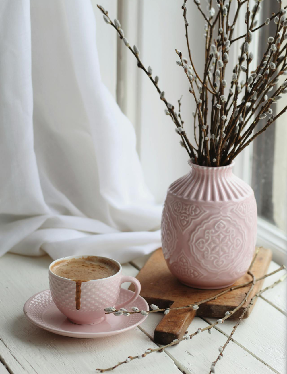 Cup of hot chocolate and a pink vase of willow stems arranged on windowsill.
