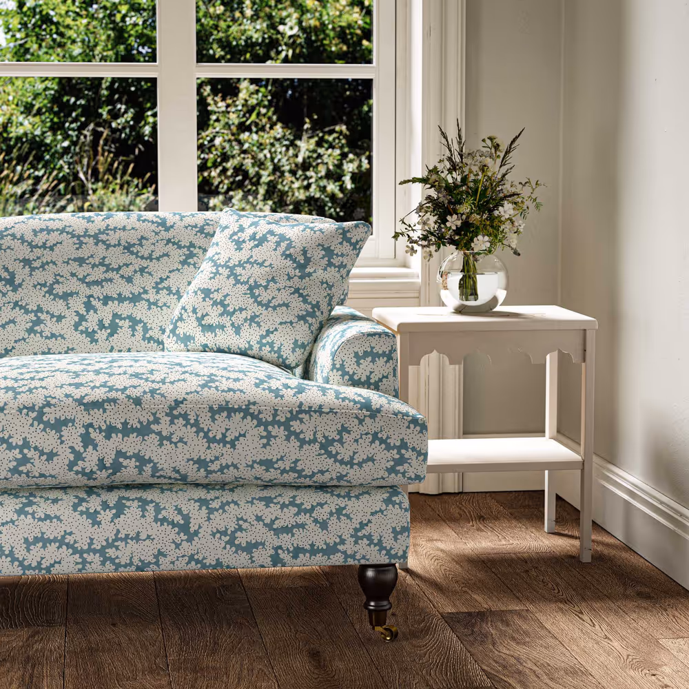 A traditional sofa in a pale sea green mini print positioned in front of a window overlooking a garden