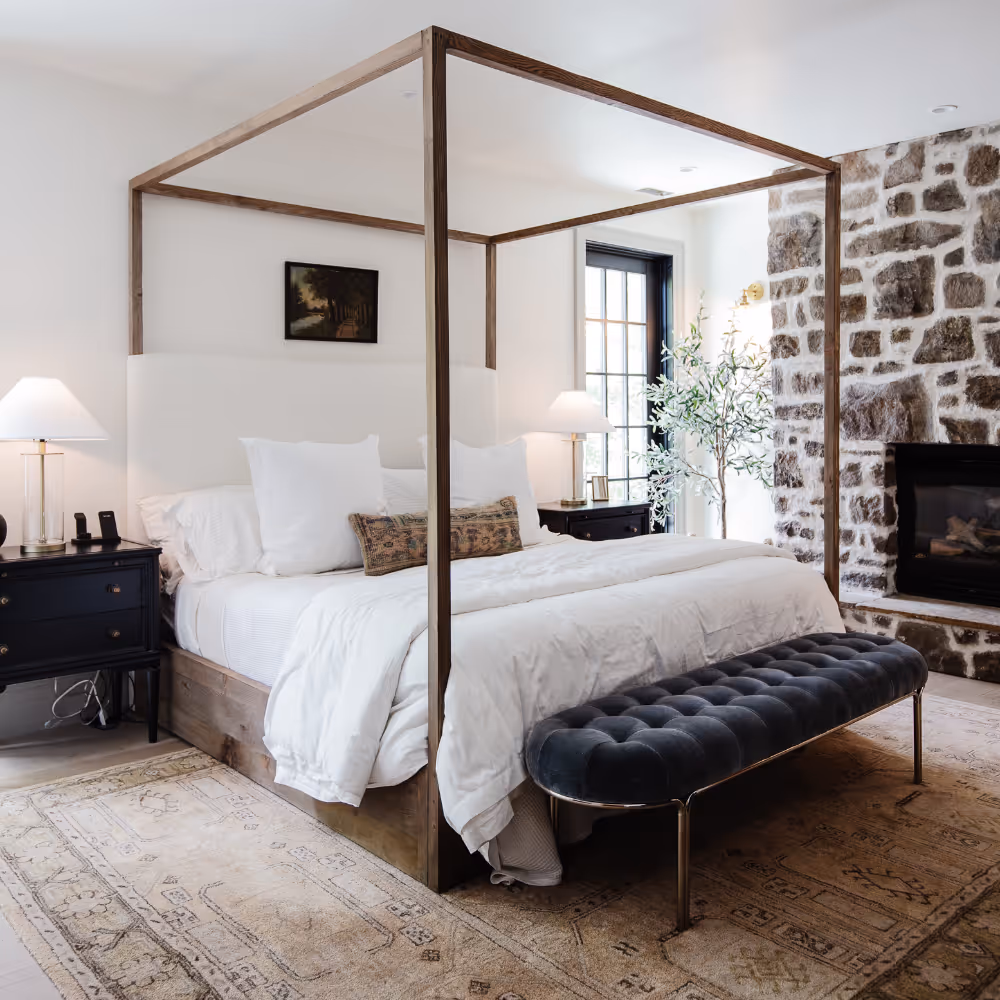 A bright and airy white bedroom with a modern four poster bed and an exposed natural stone wall