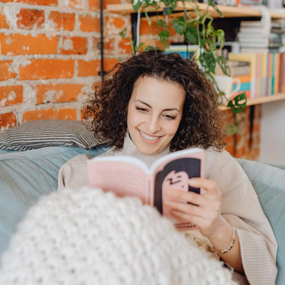A smiling woman on a sofa reading a book