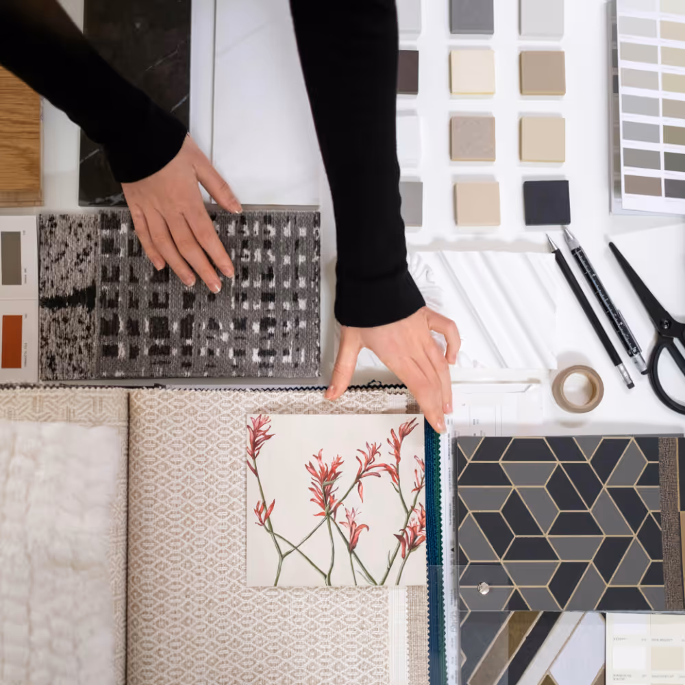 A woman laying out carpet and wallpaper samples for an interior design project.