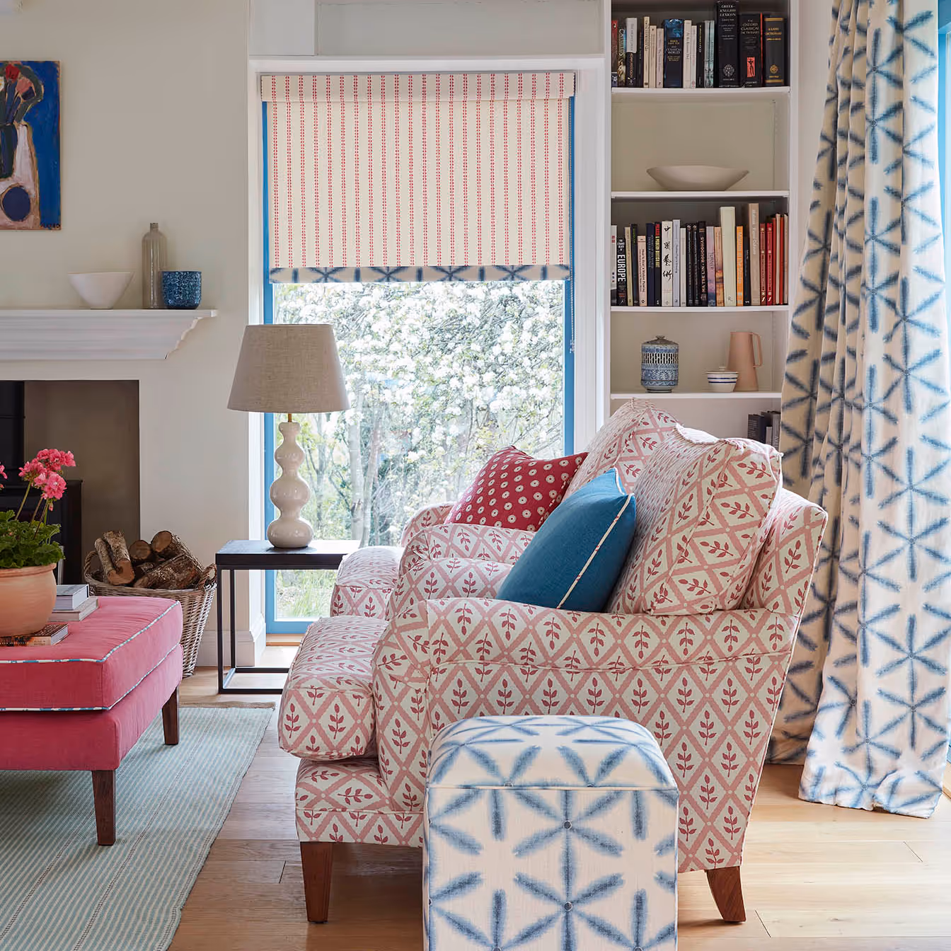 A country style living room with a pink sofa and armchair and blue and white linen curtains.